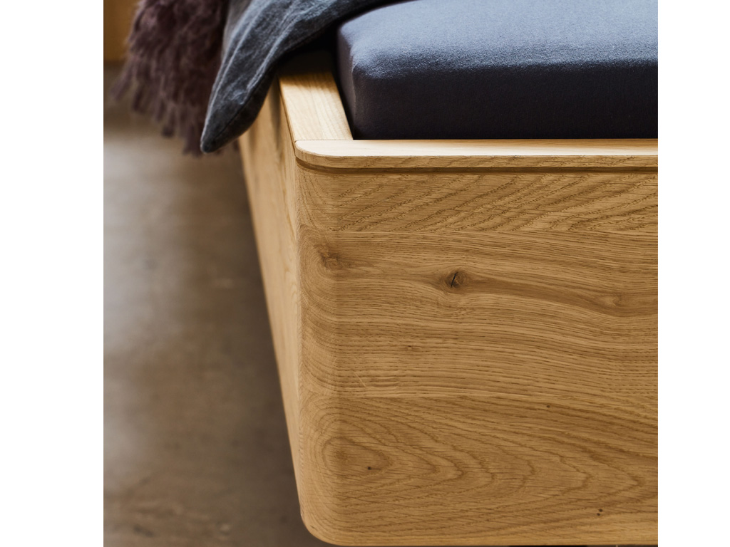 Nahaufnahme eines modernen Bettrahmens aus hellem Holz mit dunkelgrauer Matratze