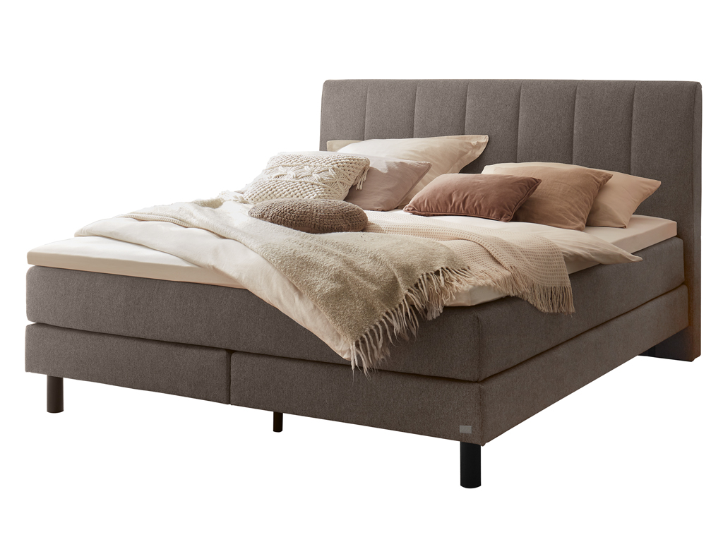 Das Boxspringbett mit schwarzem Kopfteil und grauer Stoffpolsterung, frontal vor einem weißen Hintergrund abgebildet.