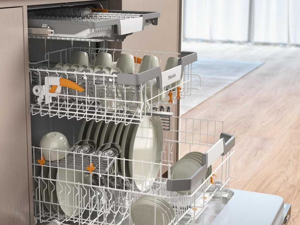 Innenansicht eines geöffneten Miele Geschirrspülers, beladen mit Tellern, Tassen, Gläsern und Besteck in den oberen und unteren Körben.