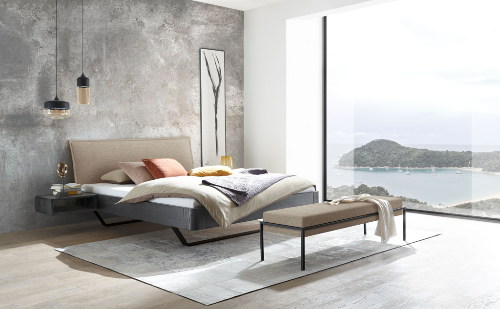 Modernes Bett mit schwarzem Rahmen und schwarzen Kufen und eine braunen Polsterkopfteil mit passender Bettbank auf Metallbeinen stilvoll dekoriert in einem modernen Zimmer