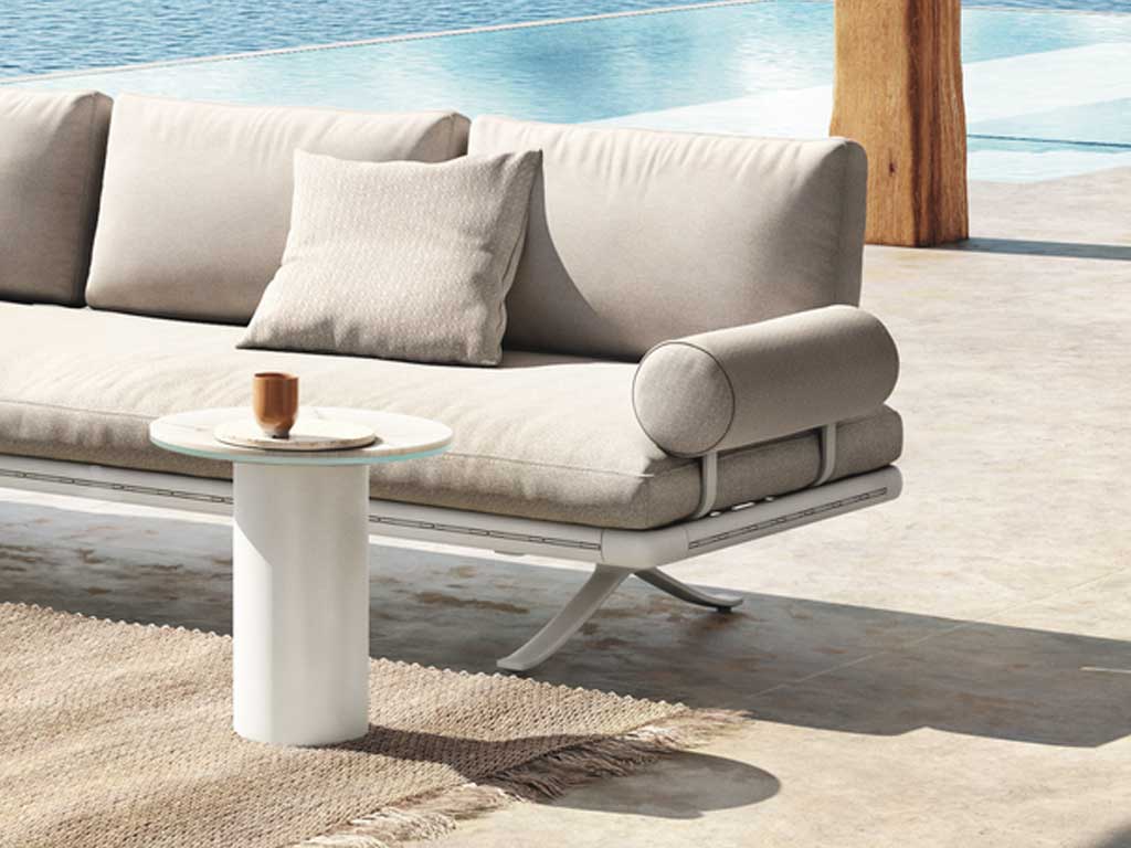 Rolf Benz Yoko 219 - Seitenteil- und Rückenbügel Modernes Outdoor-Sofa mit Kissen neben einem runden Tisch vor einem Swimmingpool auf einer Terrasse.
