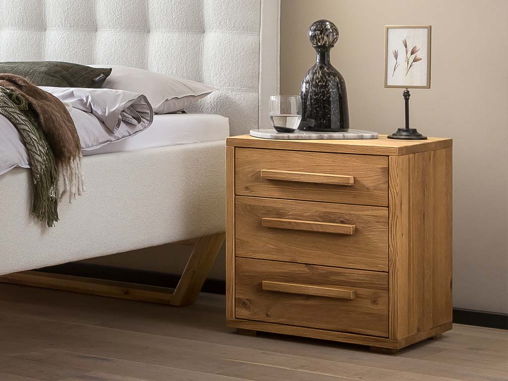 brauner Nachttisch mit drei schubladen und markanten holzgriffen stilvoll dekoriert in einem modernen zimmer stehend an einem bett turina hasena