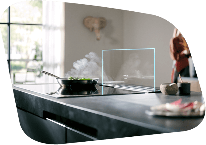 Moderne Küche mit den neusten Siemens Elektrogeräten. Eine Pfanne mit dampfenden Essen steht auf einem Siemens Kochfeld. Der Dunst wird von dem Siemens glasdraft Dunstabzug abgesaugt.