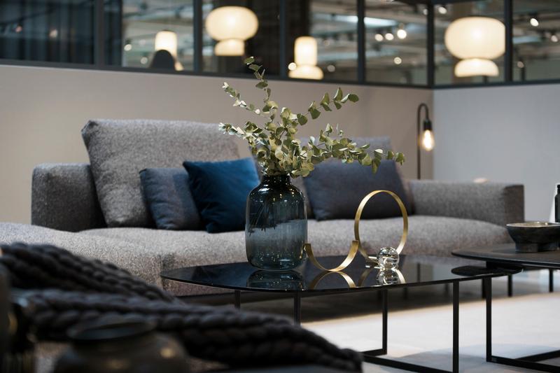 Glascouchtisch in schwarz mit Pflanzendeko und Polstermöbel im Hintergrund in grau