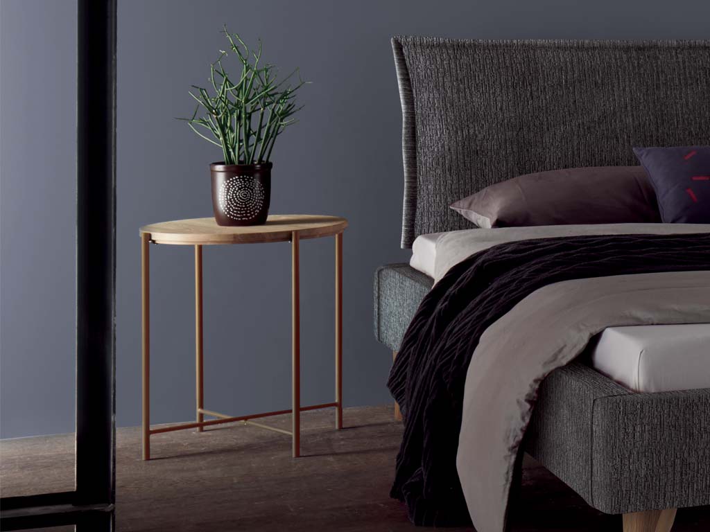 Kleiner brauner beistelltisch mit runder platte auf einem vierfüßigen metallgestell in orange stilvoll dekoriert neber einem bett vor blauer wand in einem dunklen zimmer nali von hasena