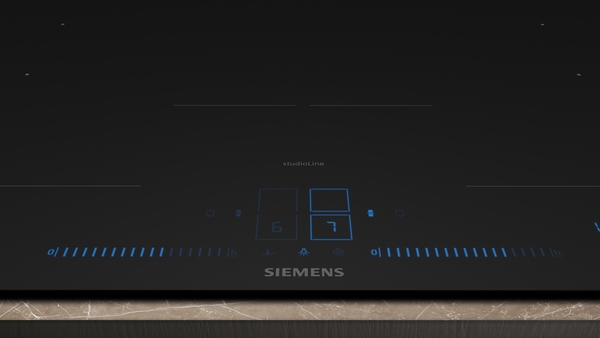 Nahaufnahme des Bedienfelds eines schwarzen Siemens studioLine Induktionskochfelds mit blauer Beleuchtung, das die digitalen Leistungsstufen 6 und 7 sowie die Touch-Slider-Steuerung anzeigt.