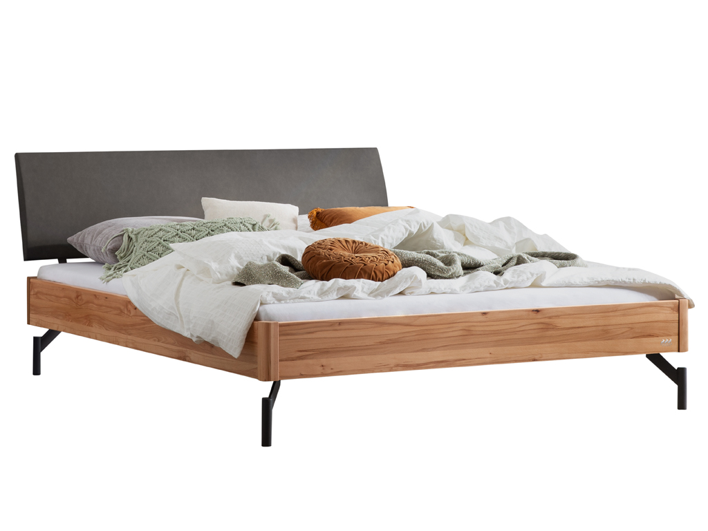 Eine Freisteller-Ansicht des Bettes "Broni" mit einem Bettrahmen aus Wildbuchenholz. Es hat ein anthrazitfarbenes gepolstertes Kopfteil und schwarze Metallfüße. Das Bett ist mit Bettwäsche und Kissen in verschiedenen Farben dekoriert.