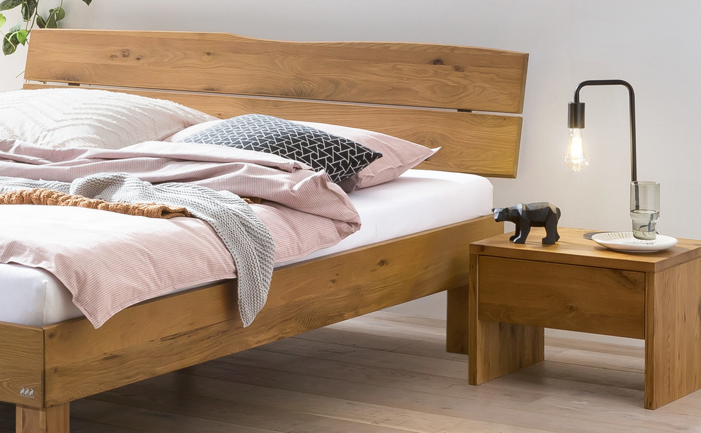 ausschnitt eines braunen Holzbettes und einem nachtschrank mit einer matratze mit weißem bezug und bettschwäsche in einem modernen zimmer hasena