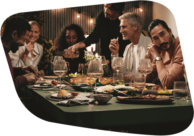 Mehrere Menschen, verschiedener Nationen essen gemeinsam an einem Tisch. Die Stimmung ist ausgelassen.