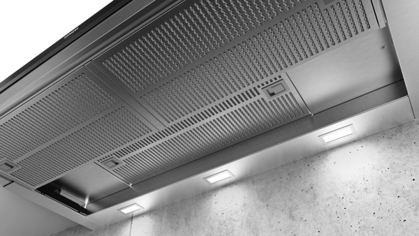 Detailansicht einer modernen Dunstabzugshaube aus Edelstahl mit eingebauter LED-Beleuchtung in einer Küchenumgebung.