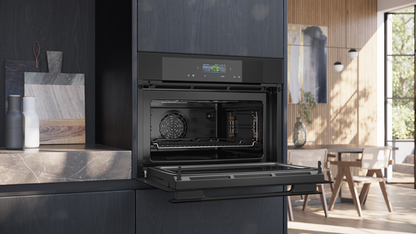 Geöffneter Siemens Kompaktbackofen mit Mikrowelle in einer dunklen Küchenzeile; ein Backblech ist auf den Schienen eingeschoben, das digitale TFT-Display ist aktiv.