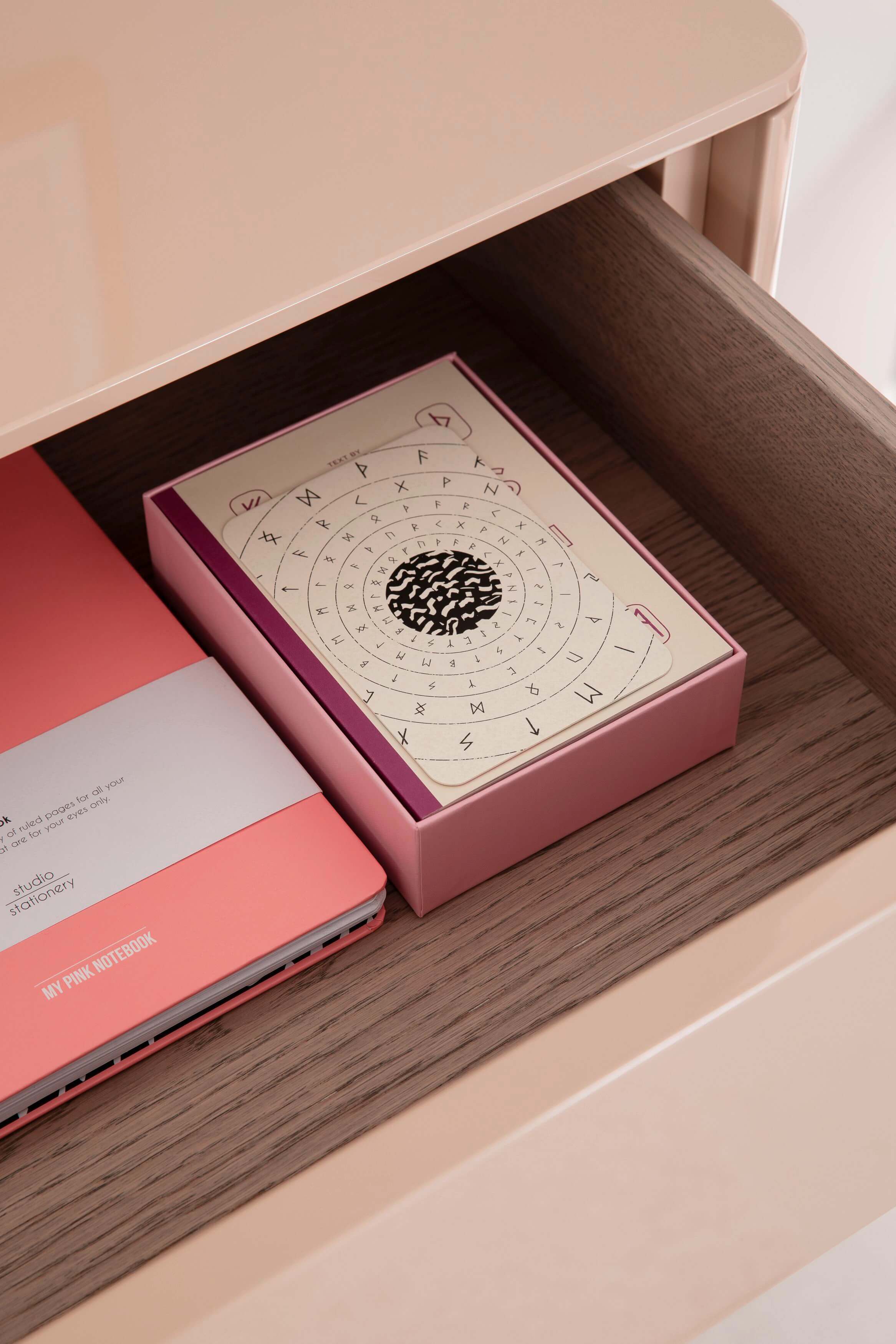 Ein rosa Notizbuch und eine Kartenbox mit Symbolen liegen in einer geöffneten Schublade auf Holz.