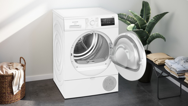 Ein Siemens Wäschetrockner mit geöffneter Tür in einem elegant eingerichteten Raum mit Pflanzen und gefalteter Wäsche