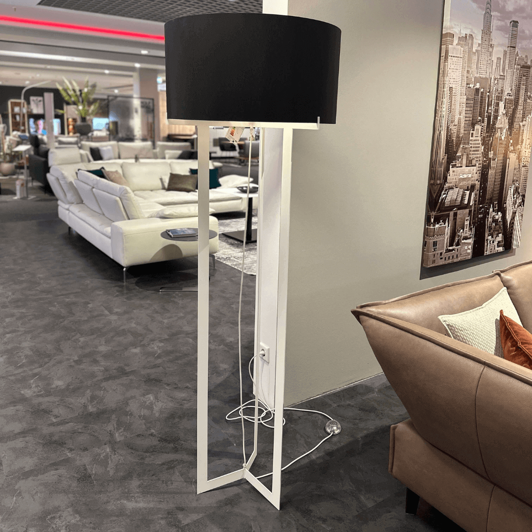 Eine moderne Stehlampe mit schwarzem Lampenschirm steht in einem eleganten Wohnzimmer mit Ledersofa und Bild an der Wand