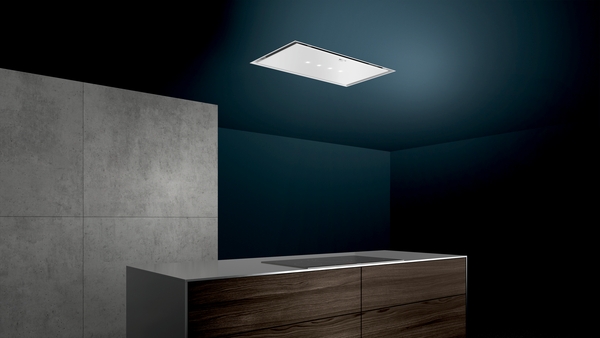 Elegante Einbau-Dunstabzugshaube beleuchtet eine moderne, dunkle Küche mit hölzernem Küchenblock und Betonwand.