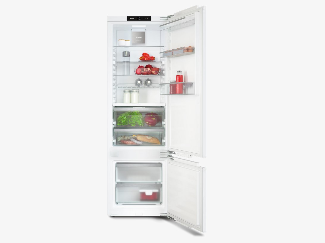 Der Miele Einbau-Kühlschrank K 7347 C mit geöffneter Tür, freigestellt auf weißem Hintergrund. Der Innenraum ist mit Lebensmitteln wie Gemüse, Milch, Eiern und Joghurt gefüllt und zeigt die flexiblen Glasablagen und die Frischeschubladen.