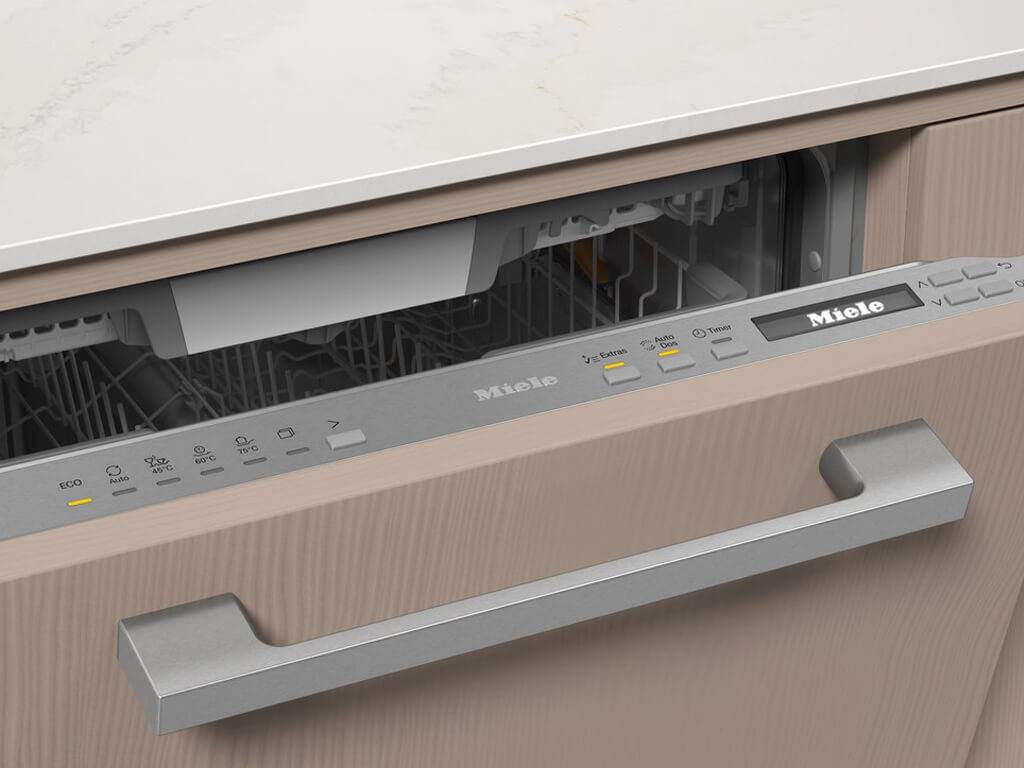 Nahaufnahme des oberen Bereichs eines geöffneten Miele Geschirrspülers, der in eine Küchenzeile mit heller Holzfront integriert ist.