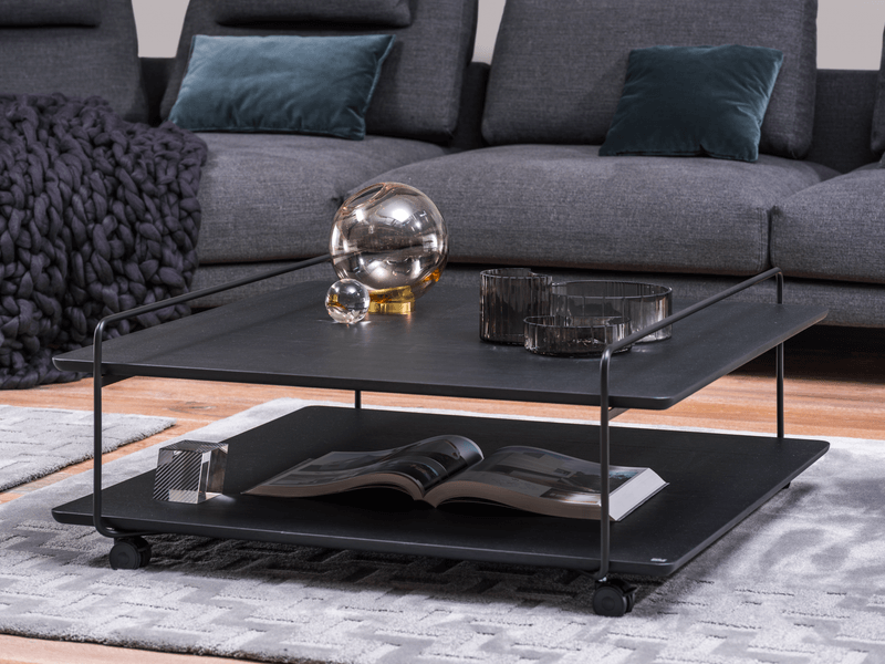 Rolf Benz 931 - Couchtisch | 102 x 100 cm schwarzer Couchtisch mit Rollen vor schwarz/grauer Couch