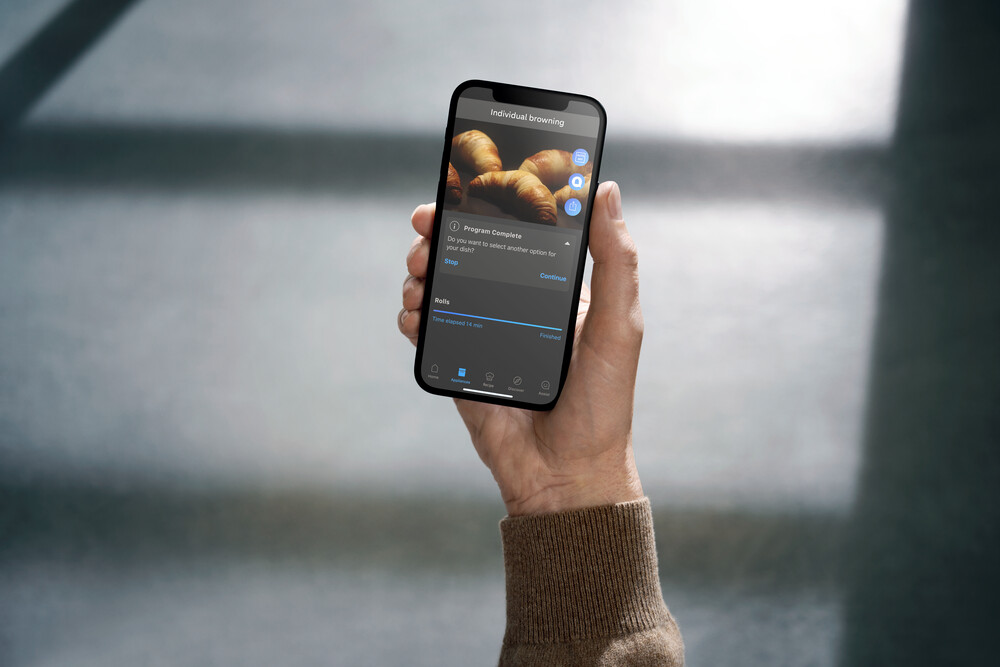 Person hält ein Smartphone mit App zur individuellen Bräunung von Croissants in der Hand