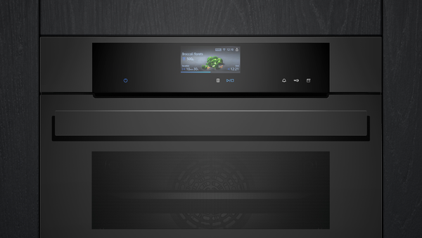 Nahaufnahme der oberen Hälfte des Backofens, eingebaut in dunkles Holz. Der Fokus liegt auf dem bündig integrierten TFT-Full-Touchdisplay Plus und dem markanten studioLine Griff.