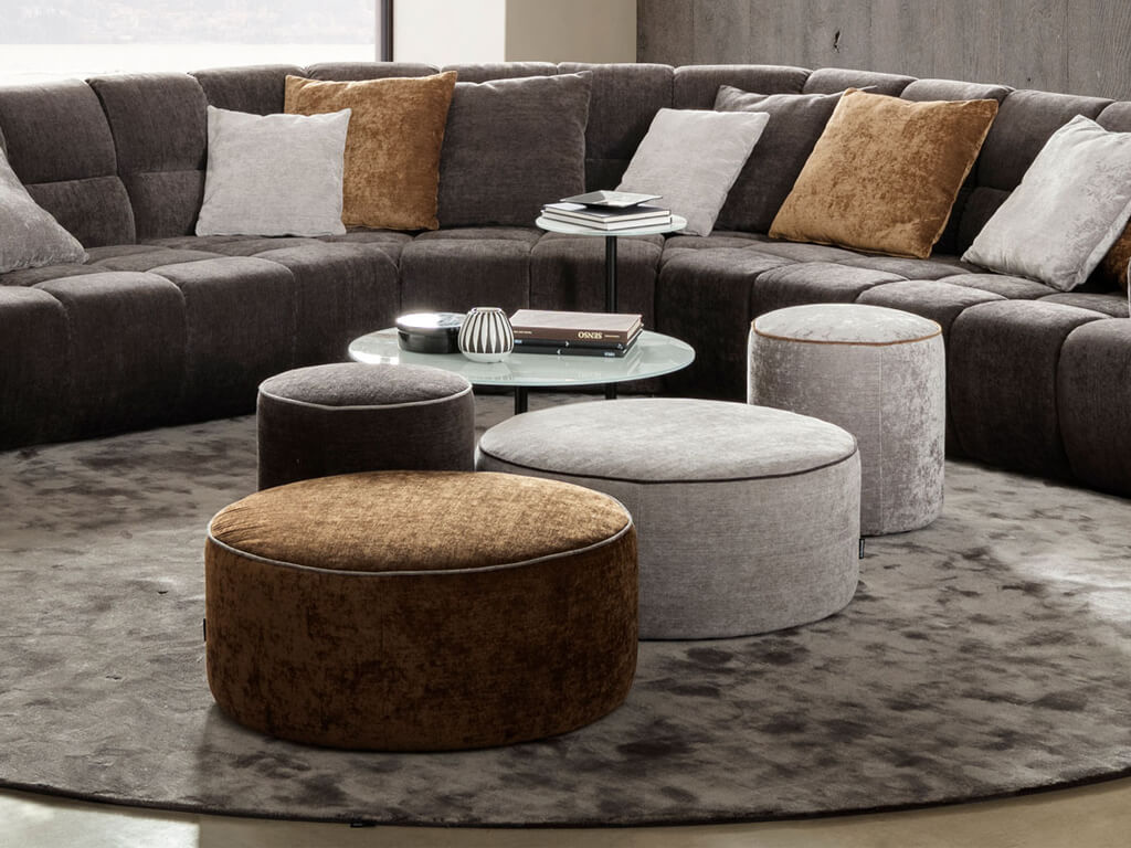 Ein elegantes Wohnzimmer mit grauer Eckcouch, runden Hockern und stilvollen Kissen auf einem Teppich