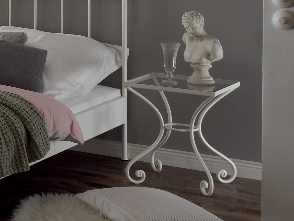 weißer Nachttisch auf filigranem Eisenmetallgestell mit Glasplatte an einem Metallbett in einem stilvollen Zimmer Cura von Hasena