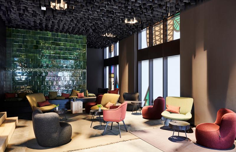 Moderne Lounge mit bunten Sesseln, grüner Ziegelwand und kreativem Deckendesign in einem hellen Raum
