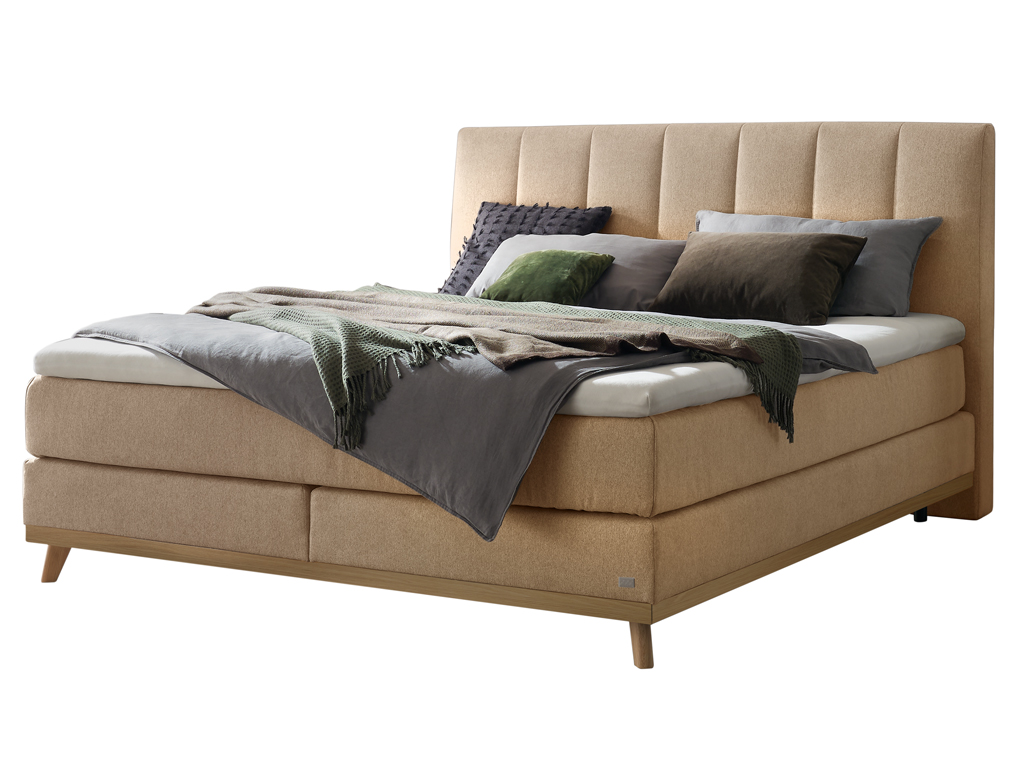 Ein freigestelltes Produktfoto des Hasena Boxspringbettes Pronto Stefania mit einem sandfarbenen Stoffbezug, dekoriert mit Kissen und einer Decke.