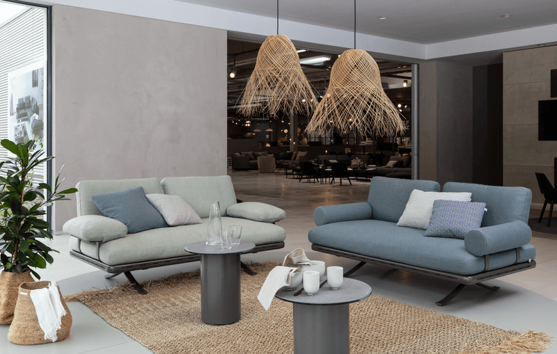 Elegantes Wohnzimmer mit einem hellgrünen und einem blauen Sofa, dekoriert mit Kissen, und zwei Rattanhängelampen