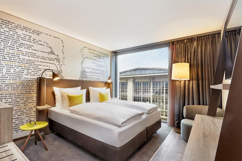 Stilvolles Hotelzimmer mit Doppelbett, Wandkunst und Blick auf Gebäude