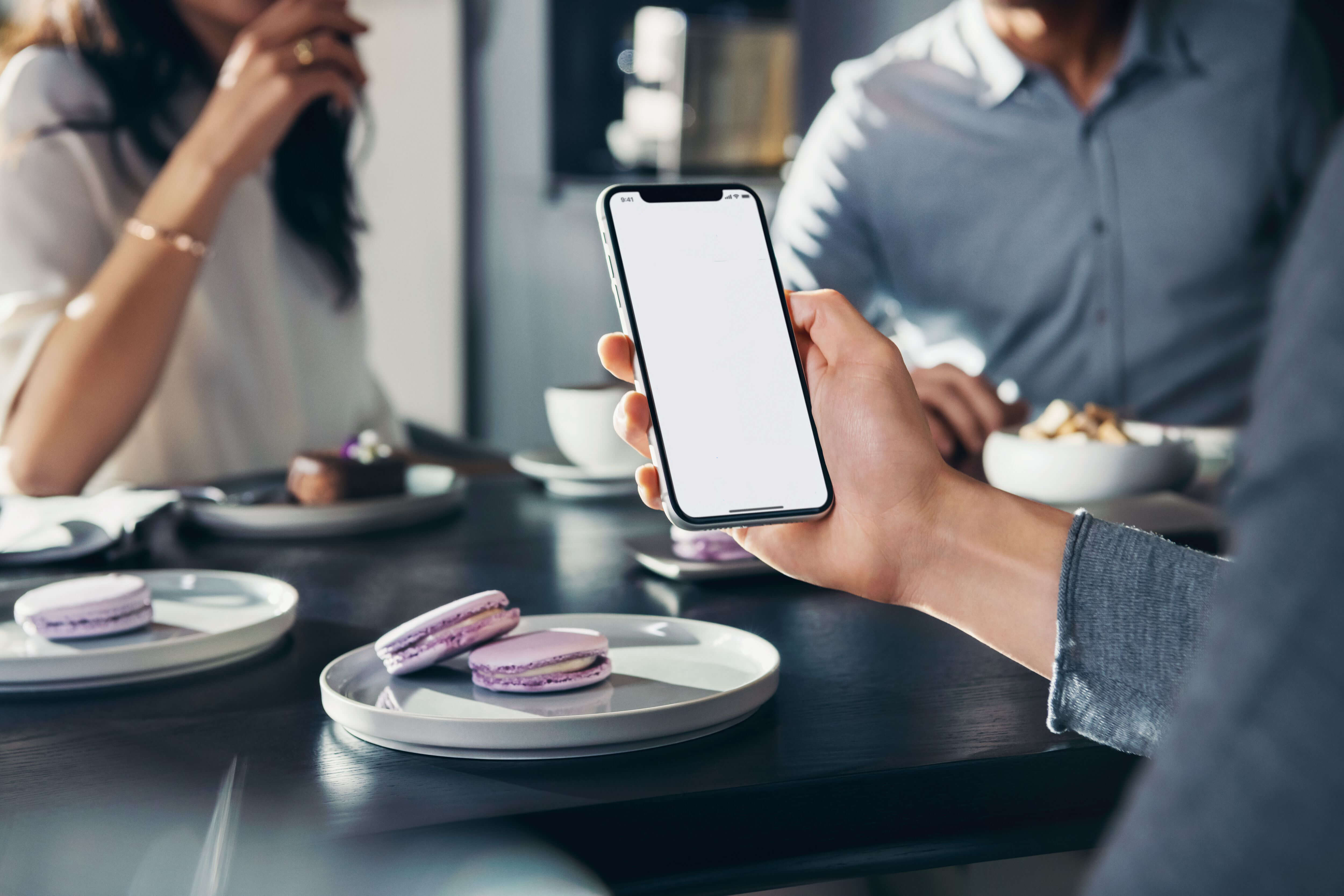 Person steuert während des Kaffeetrinkens seine Elektrogeräte zu Hause per Smartphone mithilfe der HomeConnect App. 