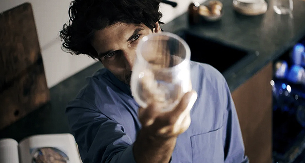 Mann hebt Glas in den Händen und prüft die Sauberkeit.