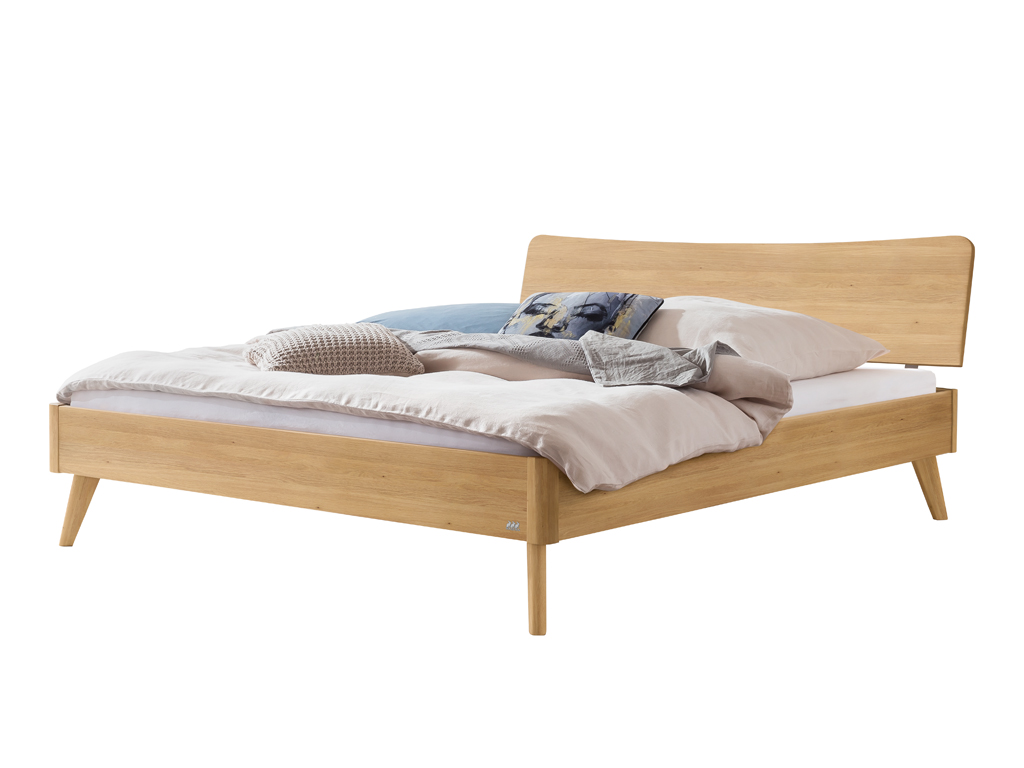 Ein freigestelltes Hasena Bett Caluso aus hellem Eichenholz ("Eiche bright"). Das Bett hat ein geschwungenes Kopfteil, schräg ausgestellte Beine und ist mit Kissen und einer Decke dekoriert.