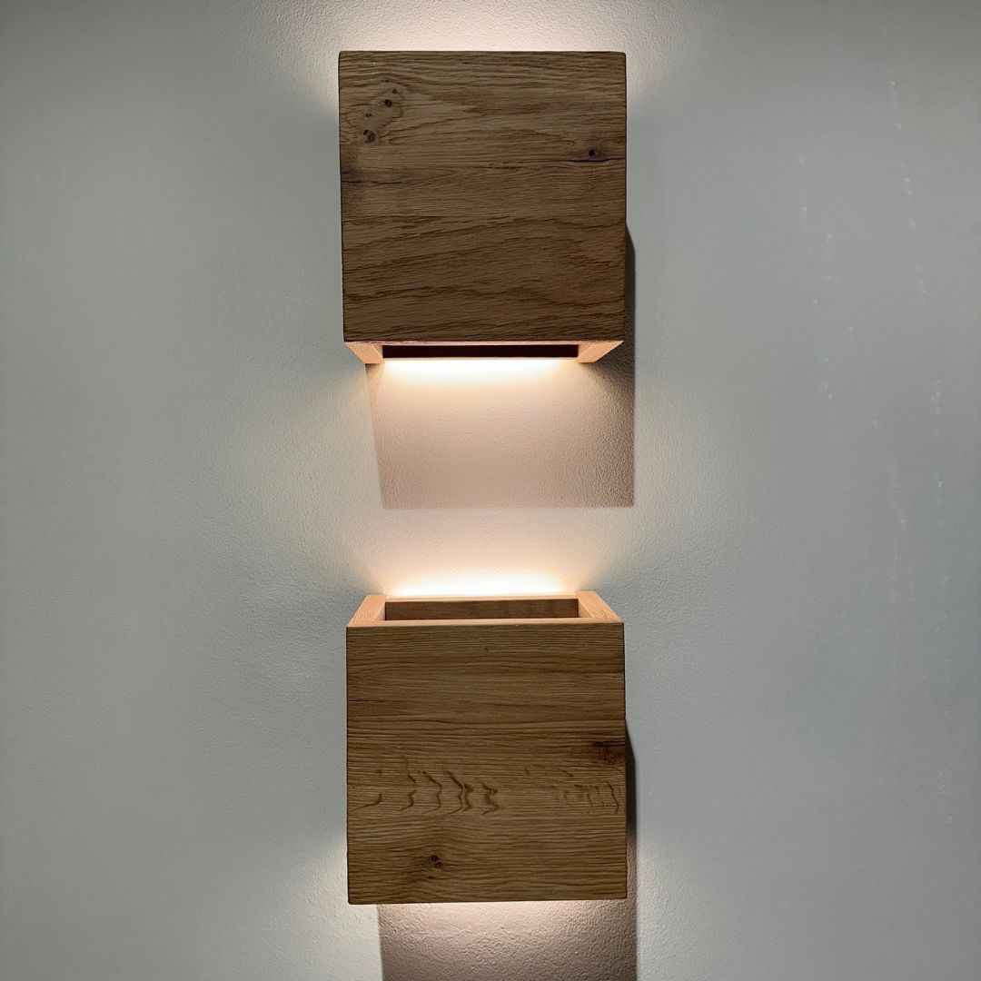 Zwei moderne, hölzerne Wandleuchten auf einer weißen Wand, die indirektes Licht nach oben und unten strahlen.