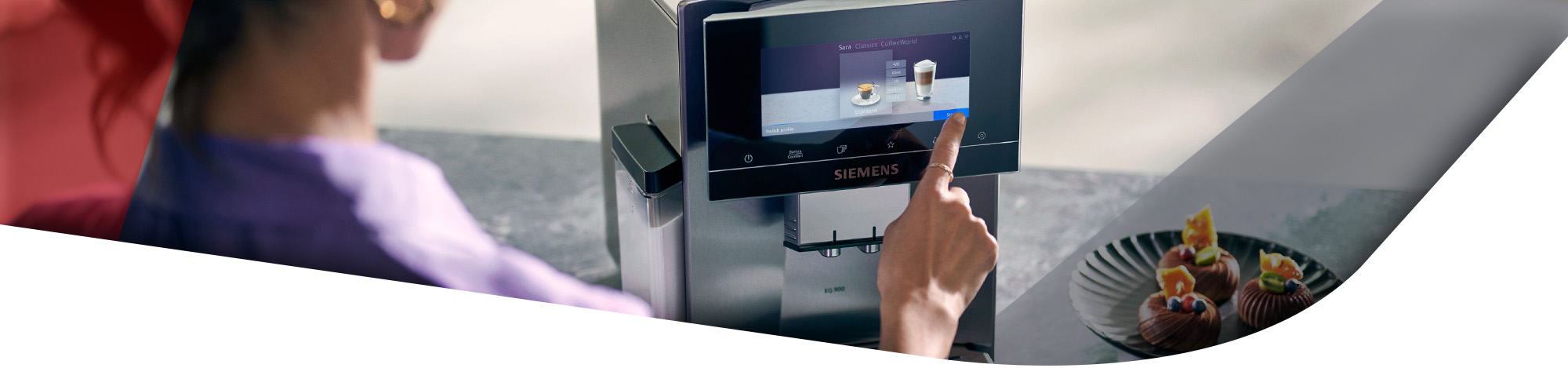 Detailaufnahme eines Siemens EQ.900 Kaffeevollautomaten. Eine Hand bedient den Touchscreen, auf dem eine Auswahl an Kaffeegetränken angezeigt wird. Rechts daneben ist ein Teller mit kleinen Schokotörtchen zu sehen.