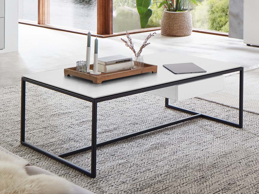 Wöstmann WM 2470 - Couchtisch | Type 9511 | B: 125,0 cm Ein moderner Couchtisch mit Glasplatte und Metallgestell in einem hellen, eleganten Wohnzimmer, dekoriert mit Kerzen und Dekorationen auf einem Tablett.