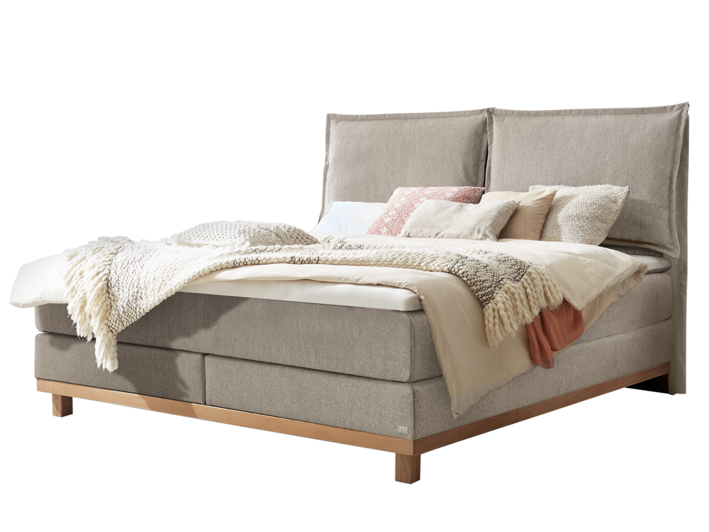 Freigestelltes, hellgraues Boxspringbett mit hellem Holzbettgestell und hoher, zweiteiliger Lehne.