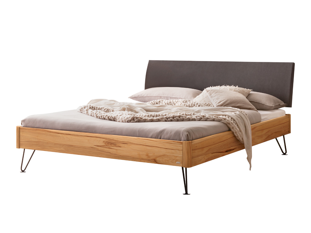 Freigestelltes Bett mit einem Bettrahmen aus Wildbuche, einem anthrazitfarbenen Kopfteil und schwarzen, schmalen Haarnadelbeinen. Das Bett ist mit heller Bettwäsche und einem groben Strickplaid dekoriert.