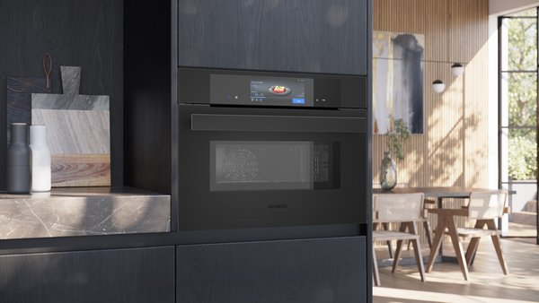 Ein eingebauter, schwarzer Siemens StudioLine Kompaktbackofen in einer dunklen Holzküche.