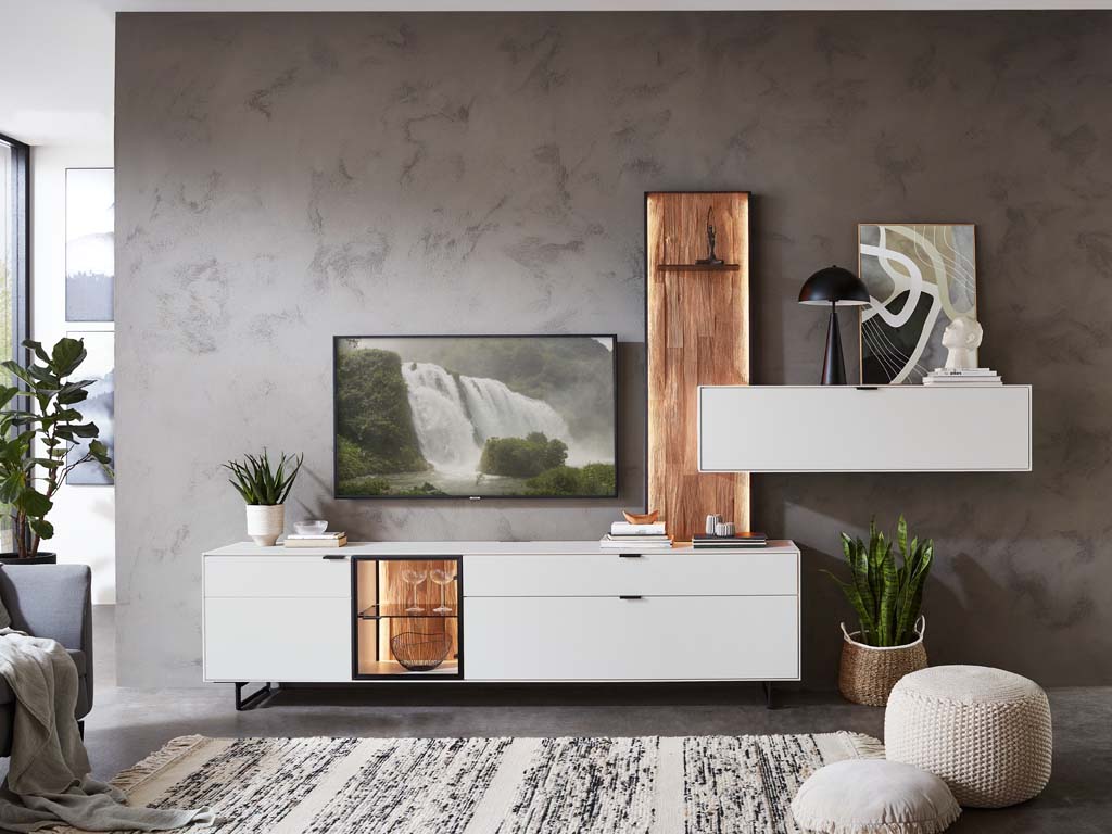 Wöstmann. WM 2470 | Wohnwand  | Type 0004/0104 Ein modernes Wohnzimmer mit einer Kombination aus weißen Möbeln, Pflanzen, einem Teppich und dekorativen Elementen an der Wand.