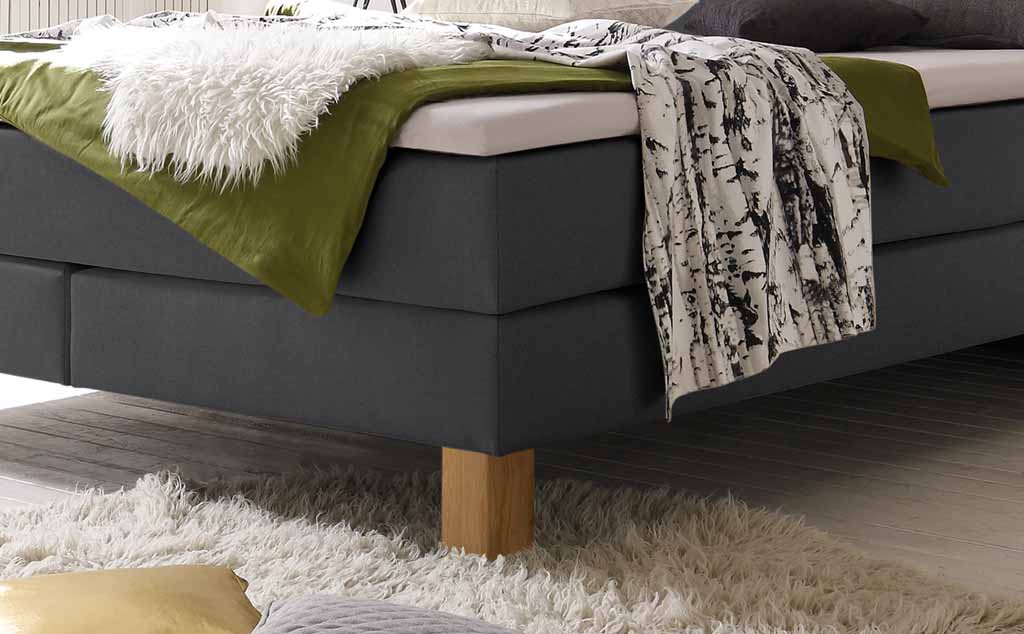 Modernes, graues Boxspringbett mit farbenfrohen Textilien und Holzboden