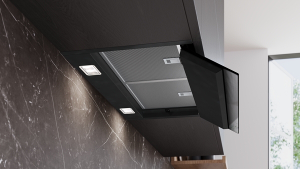 Ansicht der schwarzen Dunstabzugshaube mit heruntergeklappter Frontklappe, die die dahinterliegenden Metallfettfilter und die hellen LED-Leuchten freigibt.