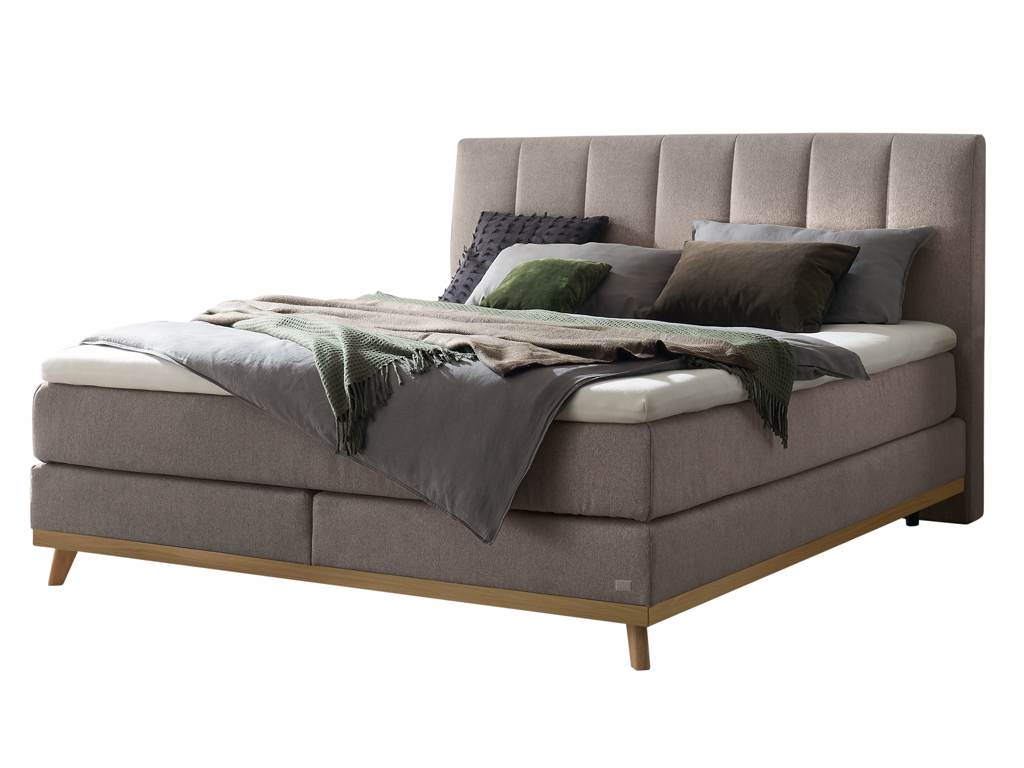 Ein freigestelltes Produktfoto des Hasena Boxspringbettes Pronto Stefania mit einem grauen Stoffbezug, dekoriert mit Kissen und einer Decke.