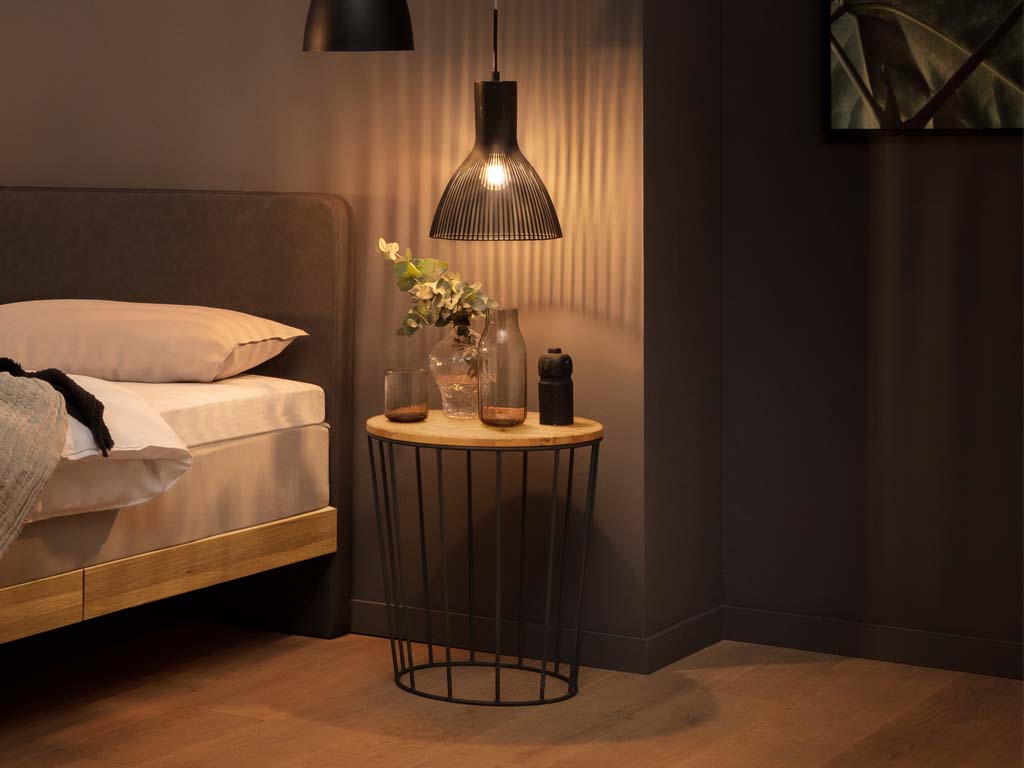 brauner runder tisch auf grauem gestell in form eines korbes in einem dunklen zimmer stilvoll dekoriert mit hängeleuchte lina von hasena