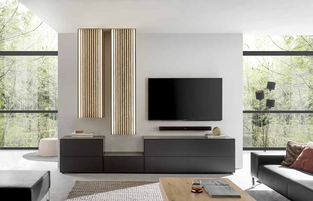 hartmann Selino - Wohnwand, 5-teilig | Type V24 | Birke/Kerneiche massiv, Lack anthrazit | B: 297,0 cm Elegant eingerichtetes Wohnzimmer mit Wand-TV, modernen Möbeln und einzigartiger Beleuchtung vor großen Fenstern
