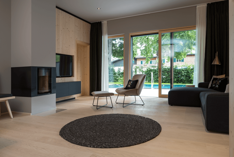 Gemütlich eingerichtetes Wohnzimmer mit Kamin, TV, Sesseln und großen Fenstern mit Gartenblick