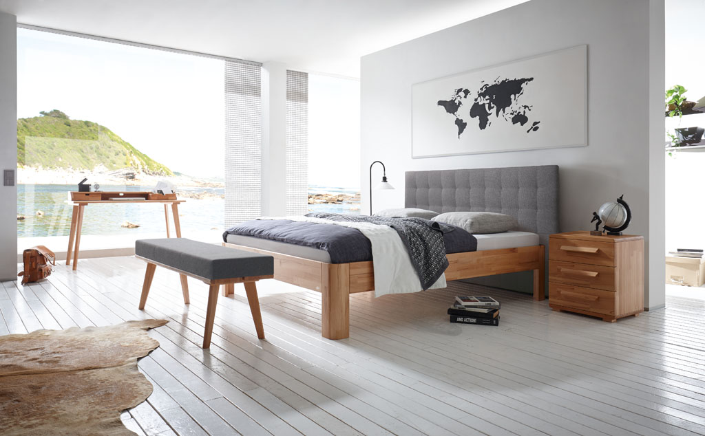 modernes Bett mit braunem Rahmen und braunen Füßen sowie eine Wandpaneel aus Polster in grau mit passender Bettbank, Sekretär und Nachtschrank stilvoll dekoriert in einem modernen Zimmer