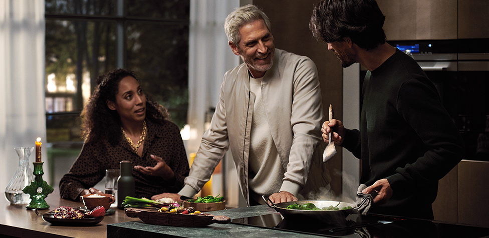 Drei Menschen stehen an der Arbeitsplatte und kochen mit dem Siemens studioLine Kochfeld mit Dunstabzug.
