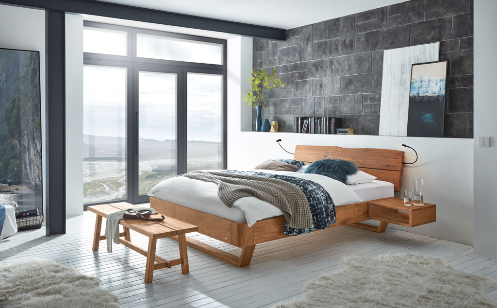 modernes Bett mit braunem Rahmen und braunen Füßen sowie eine braunem Kopfteil, passender Bettbank und Hängenachtschrank stilvoll dekoriert in einem modernen Zimmer