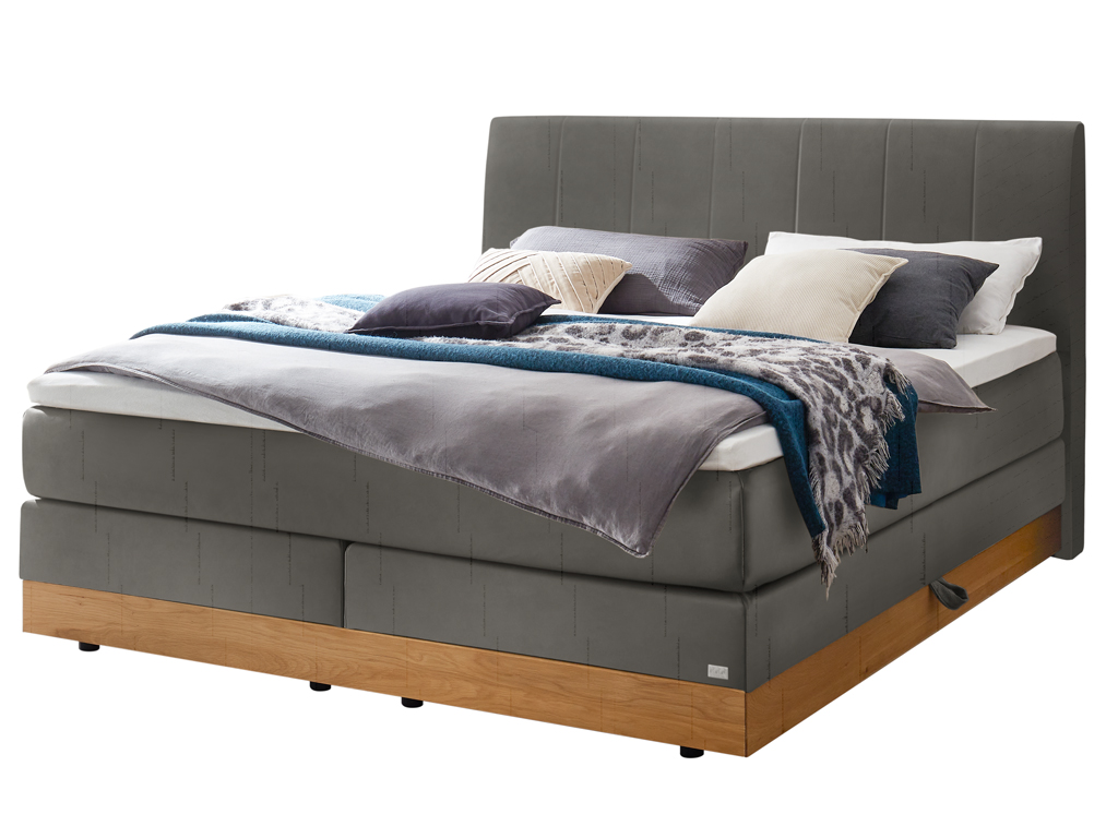 Ein Boxspringbett in dunklem Grau mit einem gesteppten Kopfteil, das auf einem Holzbettrahmen steht, freigestellt auf weißem Hintergrund.